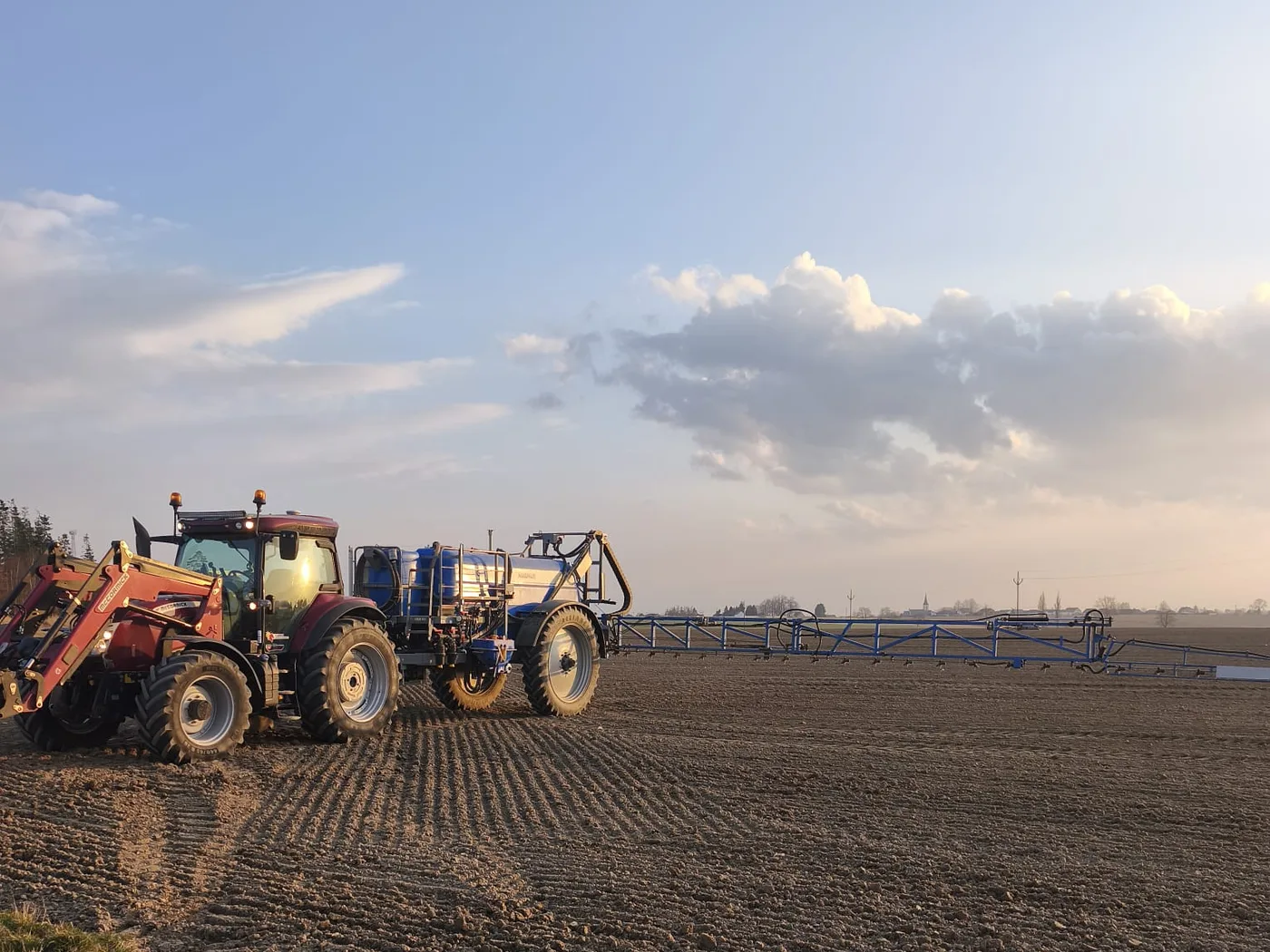 Traktor s postřikovačem na poli za soumraku